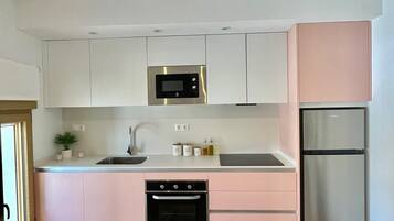 Una cocina moderna con armarios blancos y rosa, electrodomésticos de acero inoxidable y piso de madera.