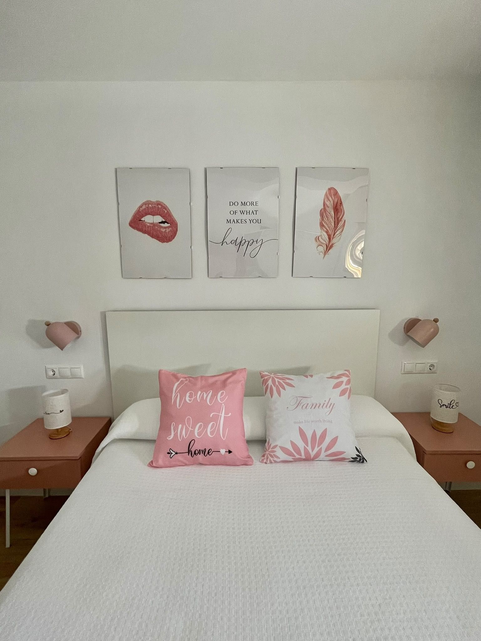 A bedroom with a bed, two pillows with text, a nightstand with a cup, and wall art.