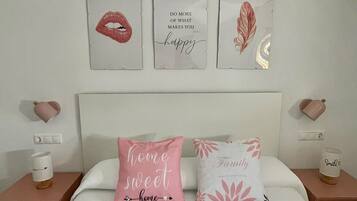 A bedroom with a bed, two pillows with text, a nightstand with a cup, and wall art.