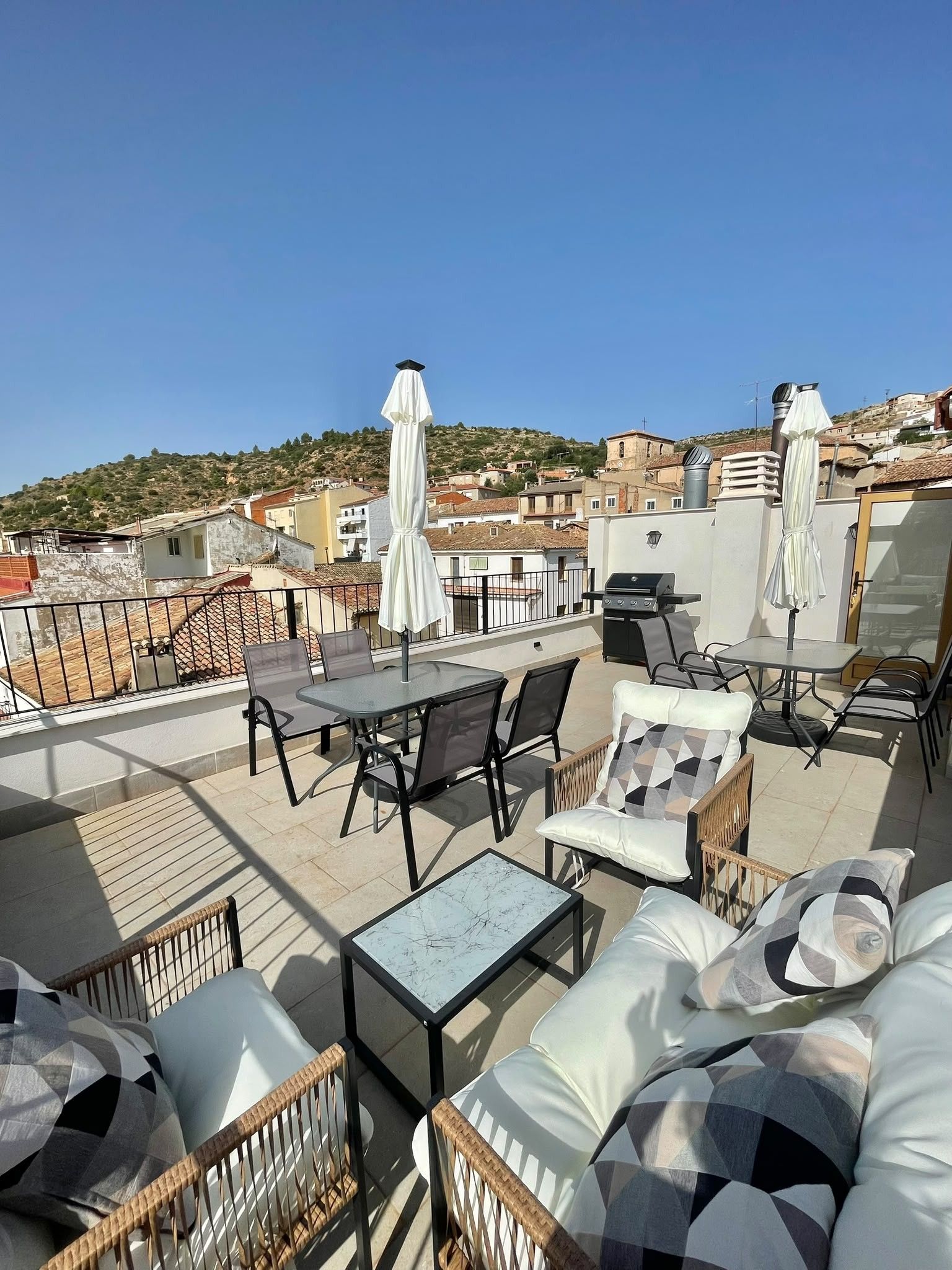 A rooftop terrace with outdoor seating, a grill, and a view of the city.