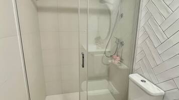 Un baño moderno con ducha envuelta en cristal, inodoro y lavamanos.