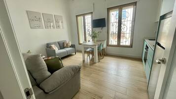 Una sala de estar moderna con un sofá, una mesa de comedor con sillas y una zona de cocina con un refrigerador.