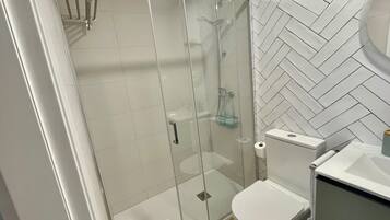 A bathroom with a glass-enclosed shower, a toilet, and a sink.