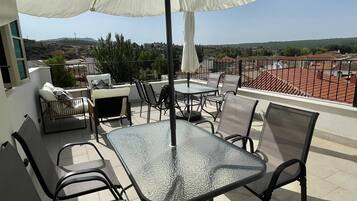 Una terraza en la azotea con mesa y sillas, un gran paraguas y vistas del paisaje circundante.