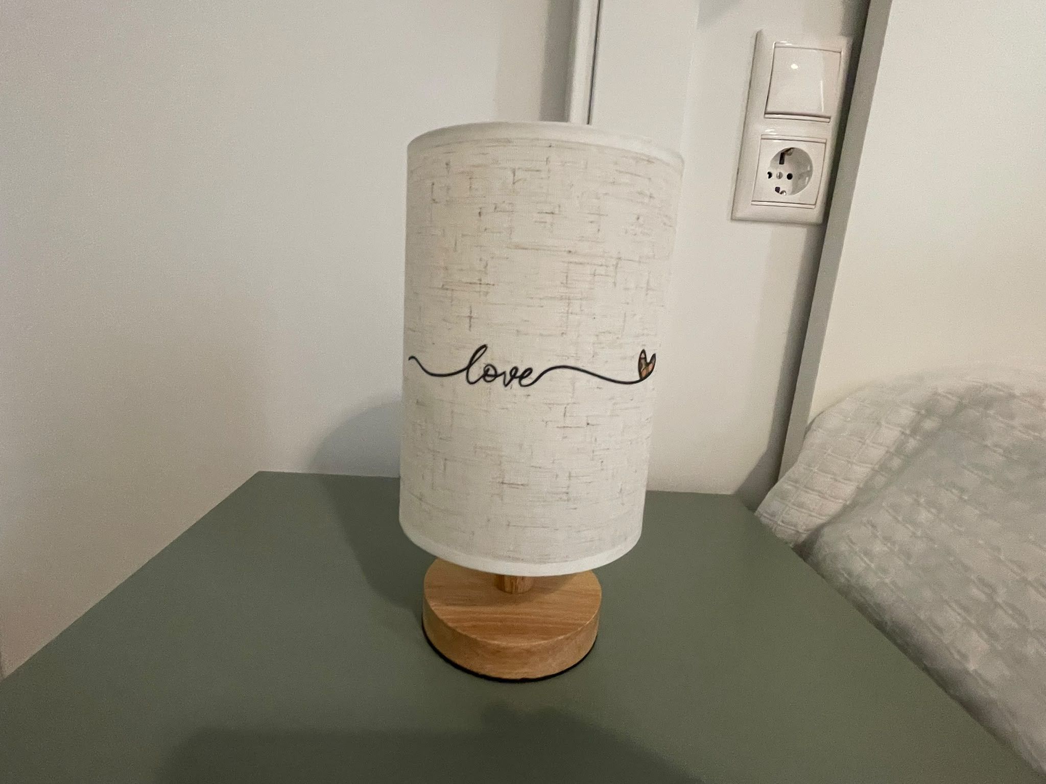 Una lámpara con pantalla blanca texturizada sobre un atril de madera, sobre una superficie verde.