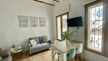 Een moderne woonkamer met een bank, een eettafel met stoelen, een aan de muur bevestigde televisie en een raam met uitzicht op de straat.