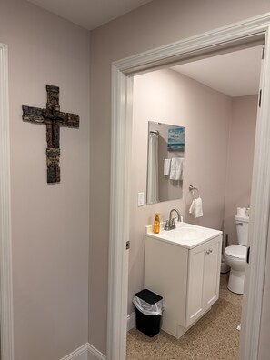Un baño con decoración de cruz, un lavamanos, un espejo, un inodoro y un cubo de basura.