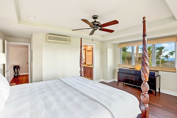 A spacious bedroom with a large bed, a ceiling fan, and a view of palm trees through the window. - Hale Hau'oli Moku by Gather - Princeville Townhome w/ 2 Cal King Suites & Pool (Princeville)