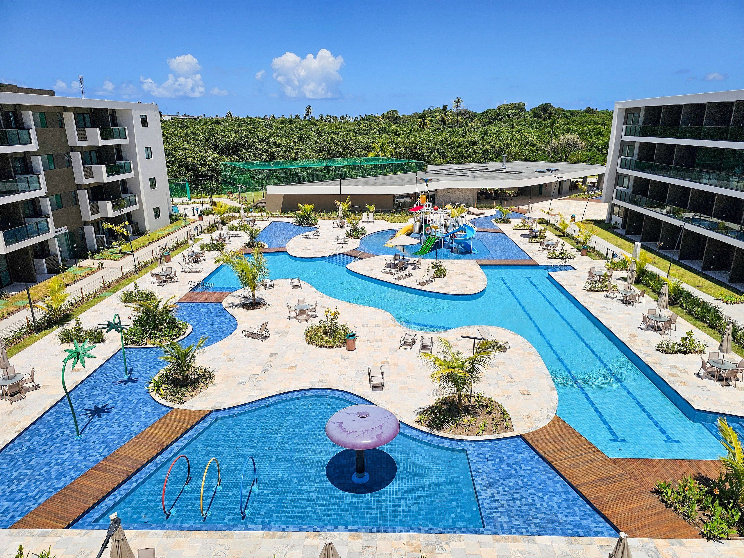 A resort pool area with multiple swimming pools, lounge chairs, and a water slide.