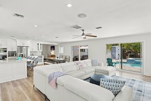 A modern living space with a white sofa, dining area, kitchen, and a view of a swimming pool. - Pool Home - Close to Barefoot & Bonita Beaches (Bonita Springs)