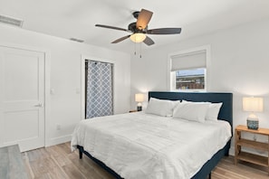 Un dormitorio con cama, ventilador de techo, ventana con persianas y puerta.