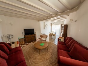 A living room with a television, a dining table, and red sofas. - Spacious, charming cottage 'Les Glycines' with Shared Pool, Private Garden and Wi-Fi (Monteaux)