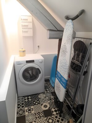 A compact laundry room with a washing machine, a drying rack, and a blue chair. - 'Les Hortensias', country-style cottage with Shared Pool, Private Terrace and Unlimited Wi-Fi (Monteaux)