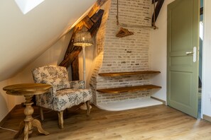 A cozy room with a sloped ceiling, a patterned armchair, a small table, and a wooden shelf. - 'Les Hortensias', country-style cottage with Shared Pool, Private Terrace and Unlimited Wi-Fi (Monteaux)