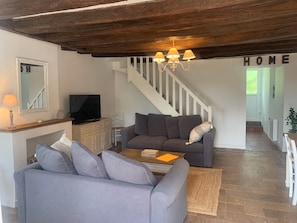 Un salon avec un canapé, une table basse, un téléviseur et un escalier.