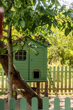 Uma casa para pássaros verde fixada em uma árvore, cercada por uma cerca de madeira.