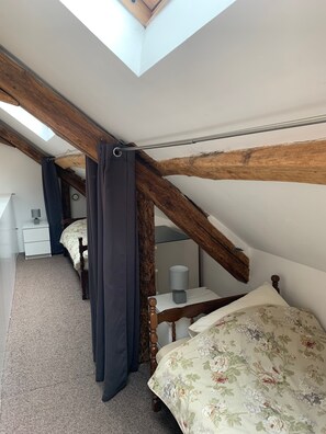 A bedroom with a sloped ceiling, wooden beams, a bed with floral bedding, a bedside table with a lamp, and a nightstand with a lamp. - Charming cottage 'Les Rosiers' with Shared Pool, Private Terrace and unlimited WiFi (Monteaux)