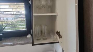 Una cocina equipada con microondas, cafetera y un armario con copas de vino y vasos.