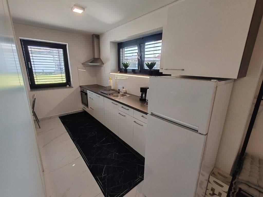 Una cocina compacta con armarios blancos, piso de mármol negro y horno empotrado.