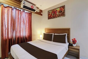 A hotel room with a bed, a nightstand, a lamp, a wall-mounted air conditioner, and a painting.