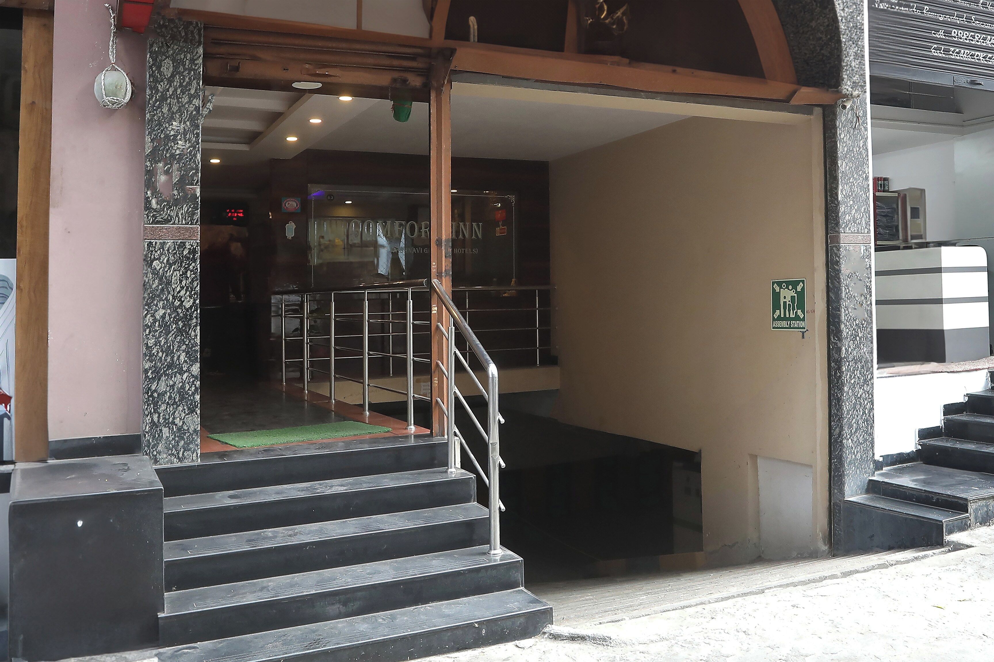 A hotel entrance with a staircase leading to the interior, a metal railing, and a sign indicating an assembly station.