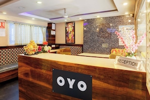 A reception desk with a sign reading 'OYO' and a 'RECEPTION' sign, a Buddha statue, and a wall with a decorative pattern.