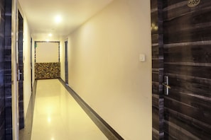 A hallway with a tiled wall, a door with a number plate, and a light fixture on the ceiling. - Hotel O Vaishnavi Inn (Hyderabad)
