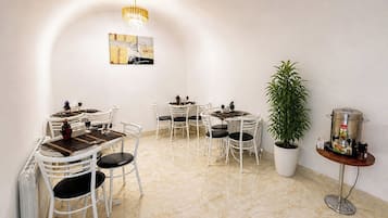 A dining area with white chairs, a round table, a potted plant, and a coffee machine.