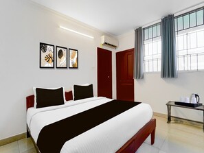 Ein Hotelzimmer mit einem Bett, einem Nachttisch mit Wasserkocher und drei gerahmten Kunstwerken an der Wand.