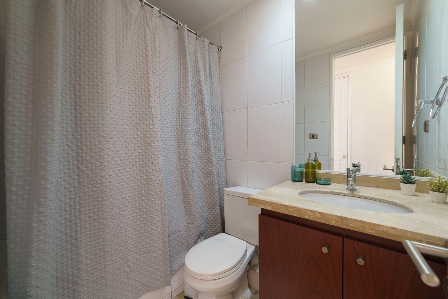 A bathroom with a shower curtain, a toilet, a sink with a mirror, and toiletries.