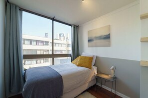 A bedroom with a bed, a bedside table, a window with curtains, and a painting on the wall. - Your Serene Getaway Central Providencia (Providencia)