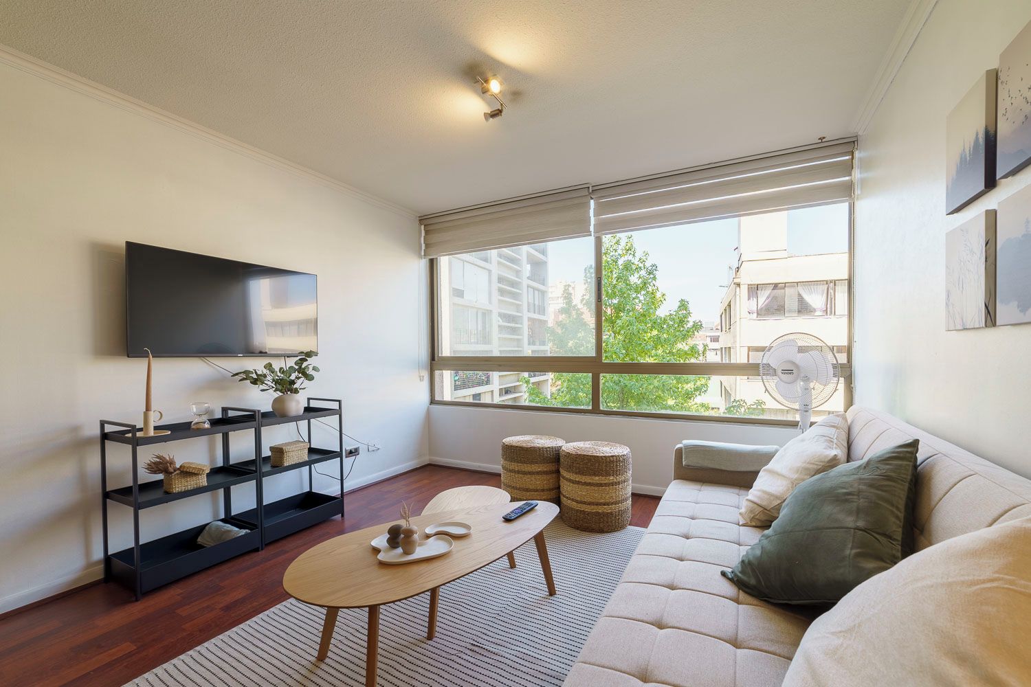 A modern living room with a sofa, a coffee table, a TV, and a window with a view of buildings and trees.