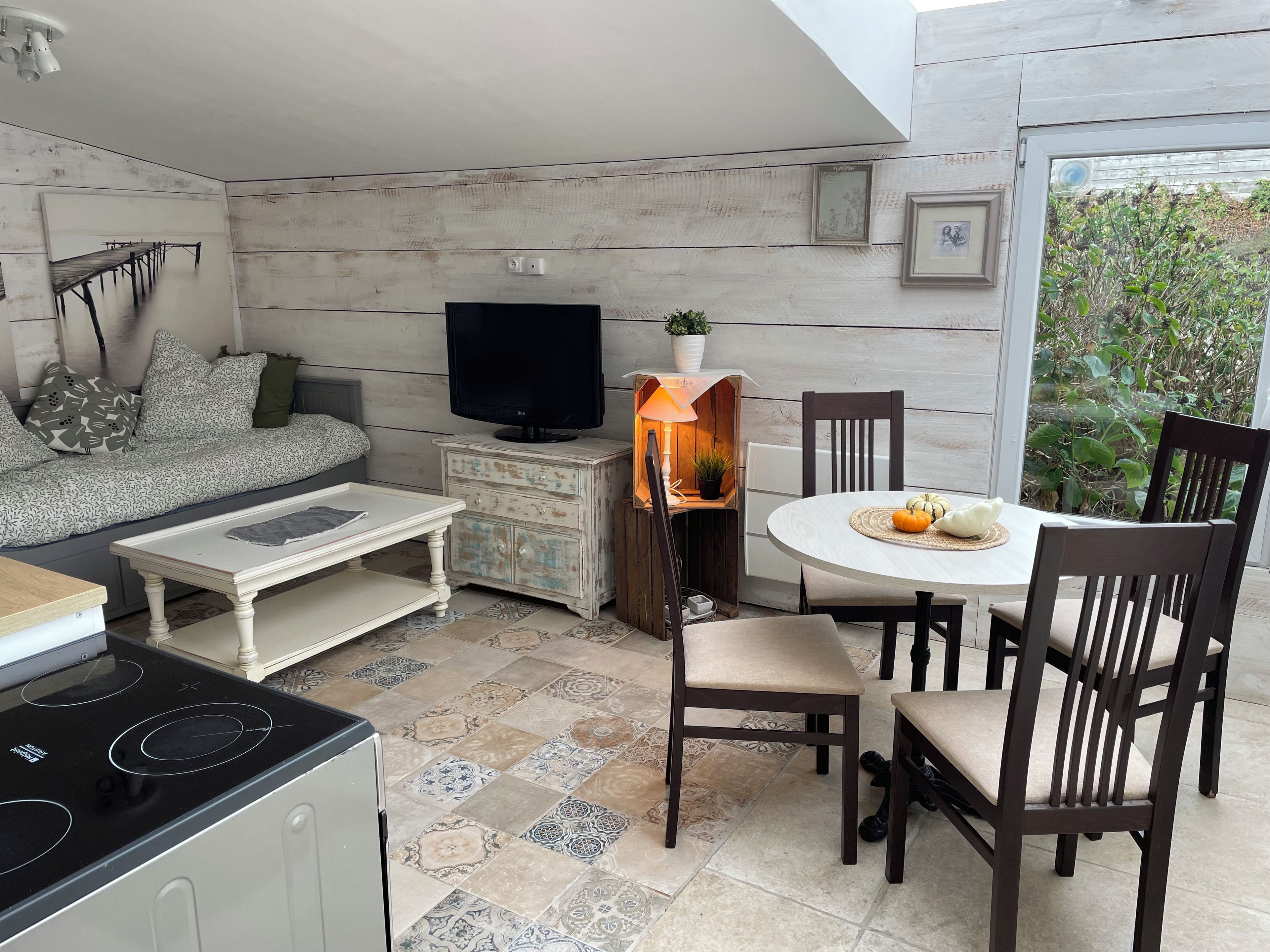 Uma sala de estar acolhedora, com sofá, televisão, mesa de jantar com cadeiras e cozinha equipada com fogão por indução.