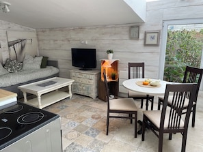 A cozy living area with a sofa, a television, a dining table with chairs, and a kitchen area with an induction stove.