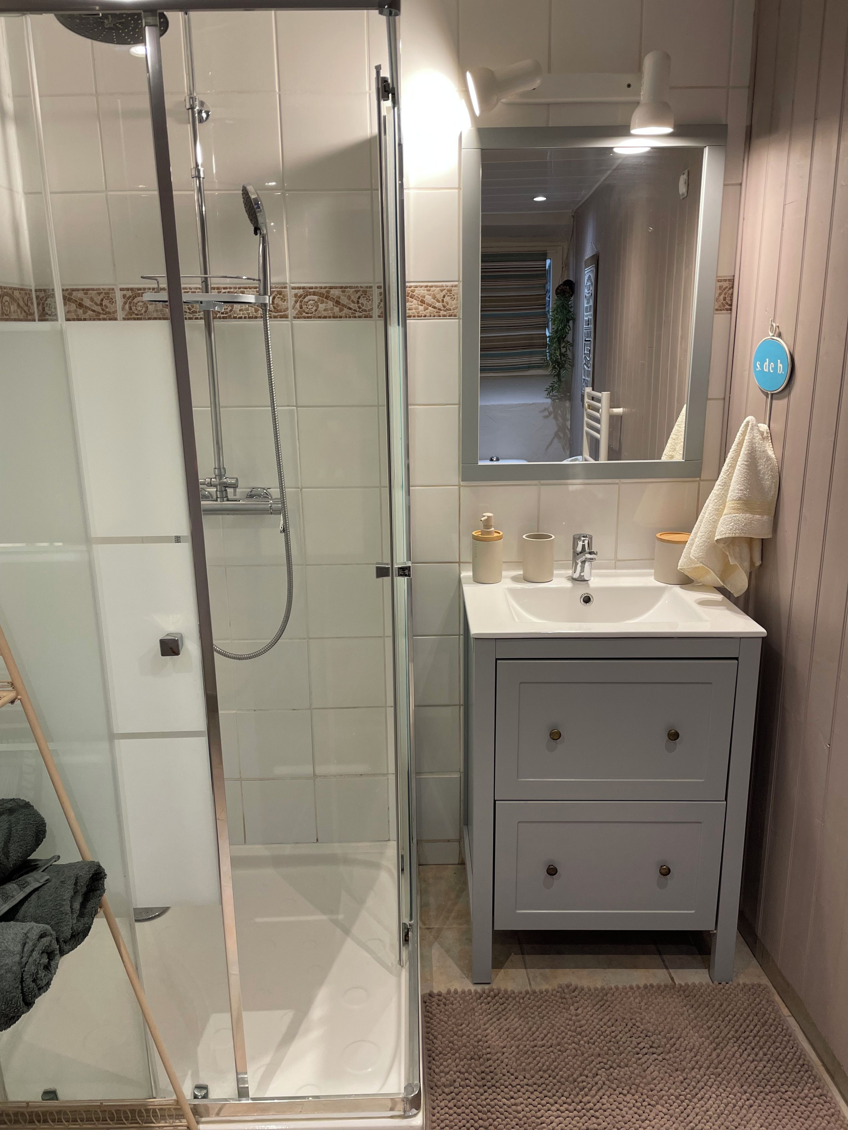Ein Badezimmer mit einer Regendusche, einem Waschbecken mit Spiegel darüber und einem Handtuch an der Wand.