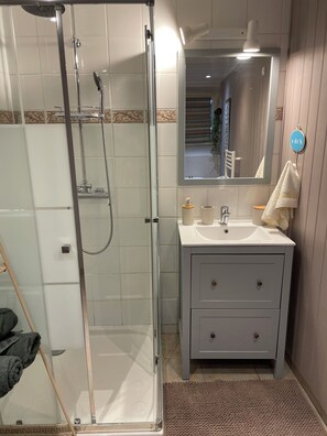 Un bany amb dutxa tancada per vidre, un lavabo amb mirall i una tovallola penjada a la paret.