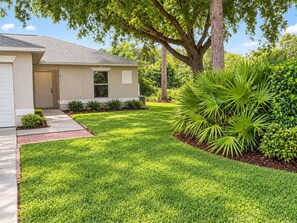 A residential house with a well-maintained lawn, a driveway, and a variety of shrubs and plants. - Spacious 3BR / 2BA Duplex Apartment - Minimum Stay 30 Days (Lehigh Acres)