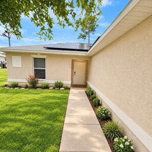 A residential house with a front door, a small porch, and a well-maintained lawn. - Spacious 3BR / 2BA Duplex Apartment - Minimum Stay 30 Days (Lehigh Acres)
