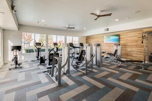 A modern gym with various exercise machines, large windows, and a wooden wall with a painting. -  Long Stays; King Bed 2BDR/2BA Suite; Private Garage (Roseville)