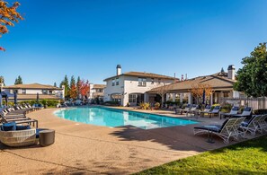 A swimming pool with lounge chairs and umbrellas, surrounded by buildings with a Mediterranean architectural style. -  Long Stays; King Bed 2BDR/2BA Suite; Private Garage (Roseville)