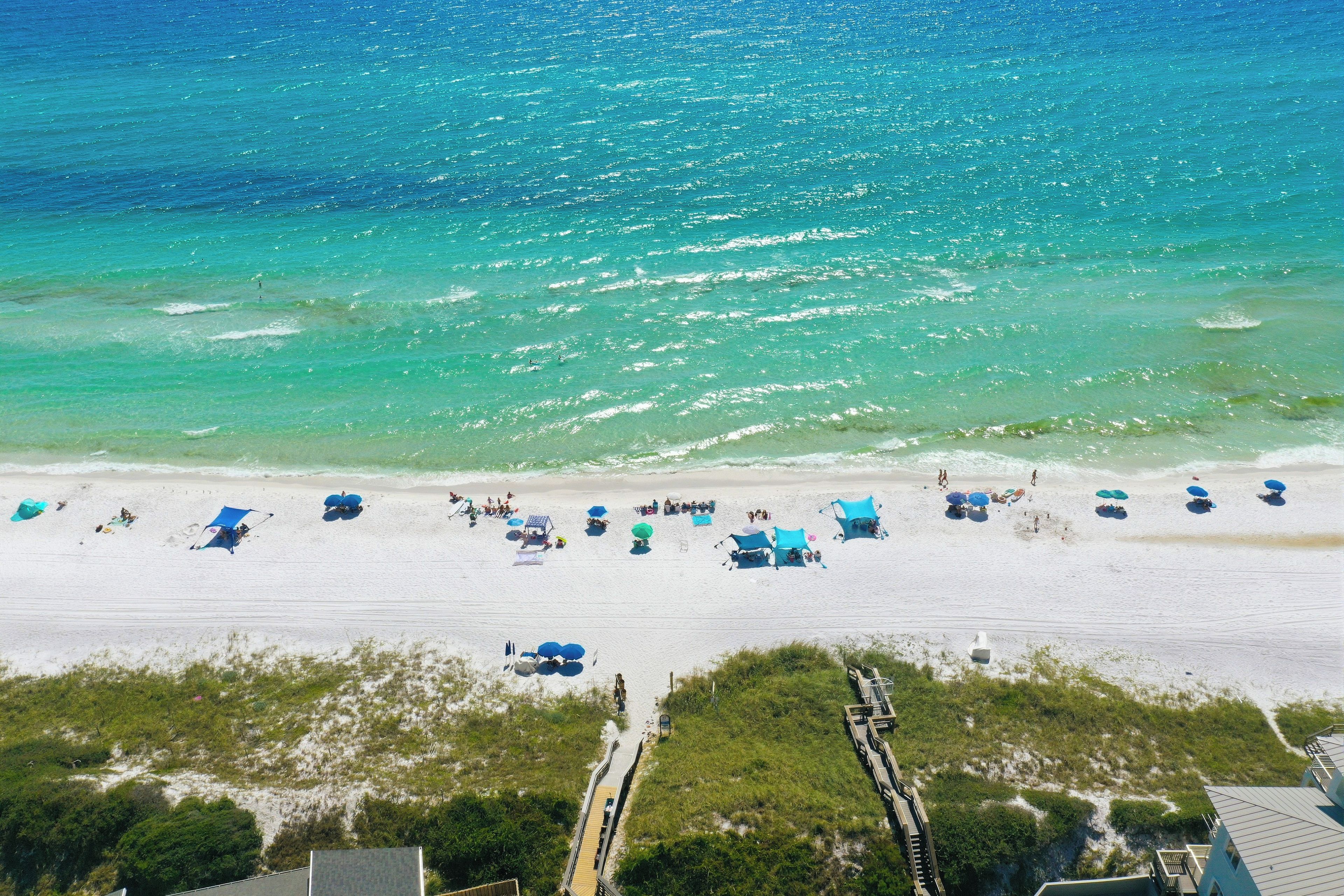 A beach with clear turquoise waters, a sandy shore, and a boardwalk leading to buildings.