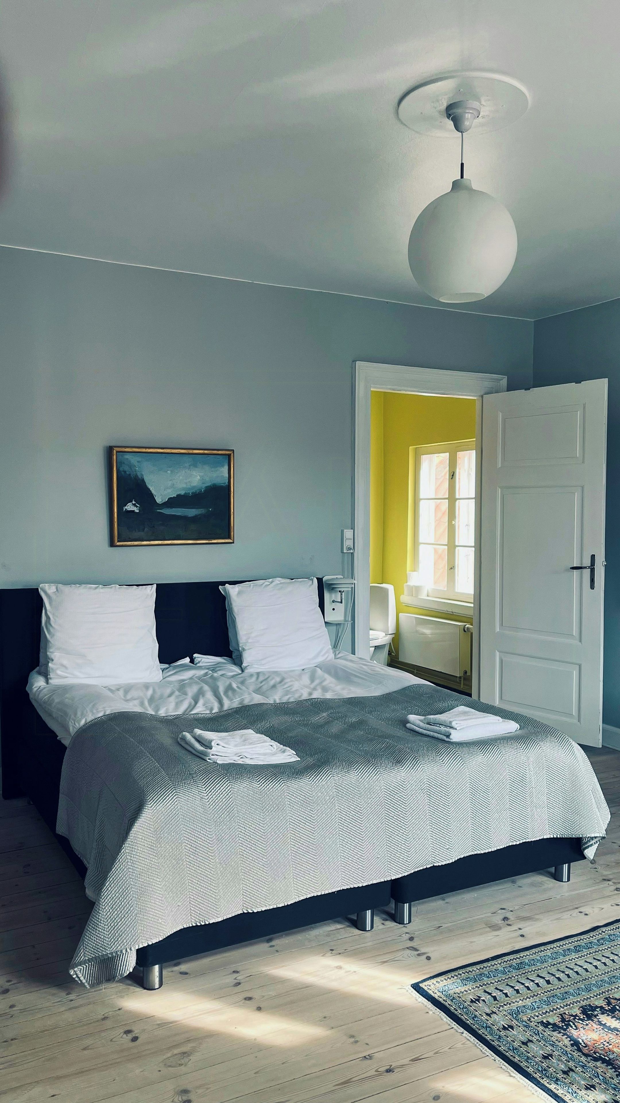 A bedroom with a bed, a painting, a door, and a window.