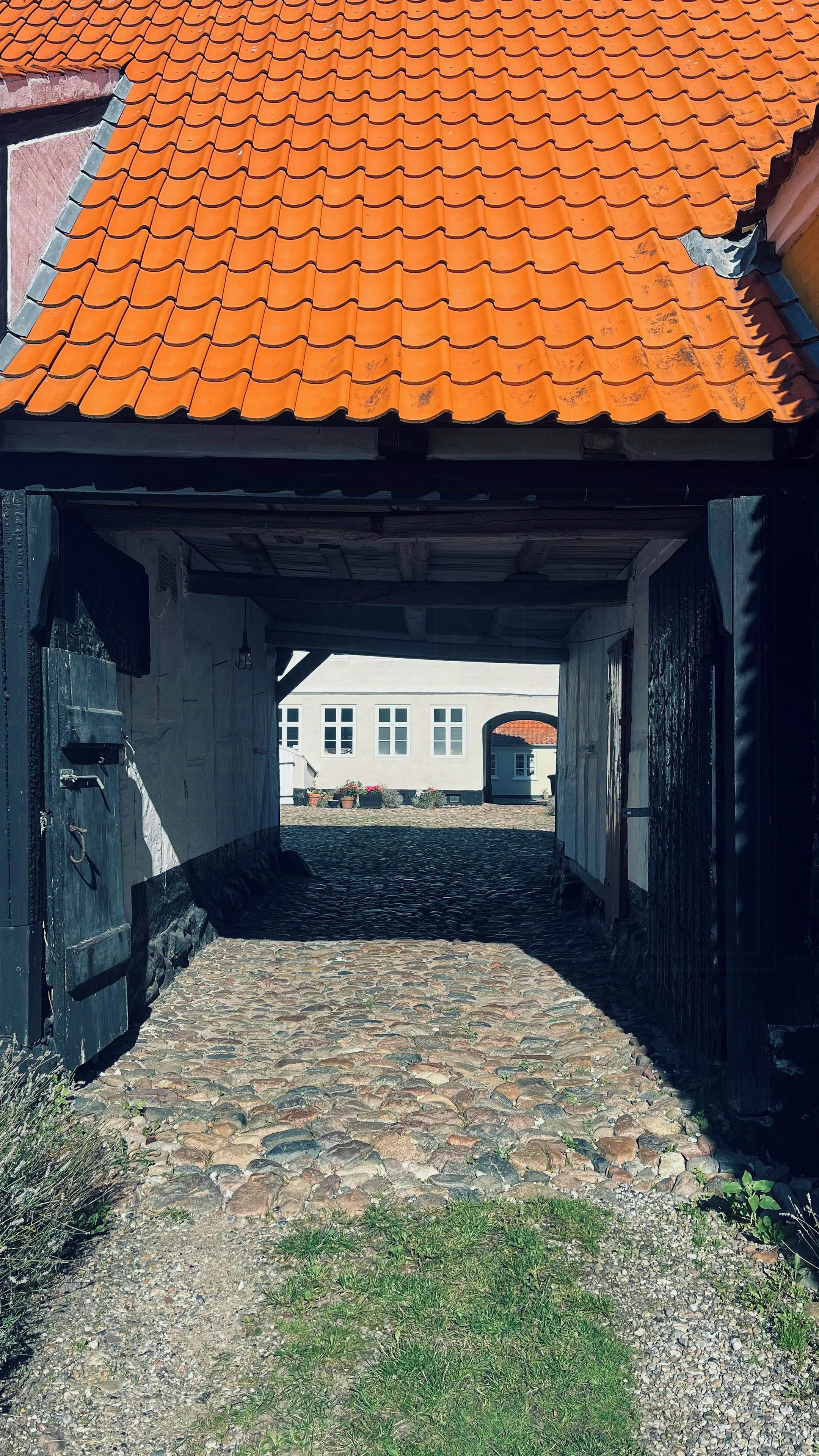 Ein Kopfsteinpflasterweg führt zu einem Gebäude mit rotem Ziegeldach und weißer Fassade.