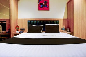 A hotel room with a large bed, a headboard with a unique design, a bedside table with a phone and a vase of flowers, and a painting on the wall. - Townhouse Oak New Nashik Highway 2 (Bhiwandi)