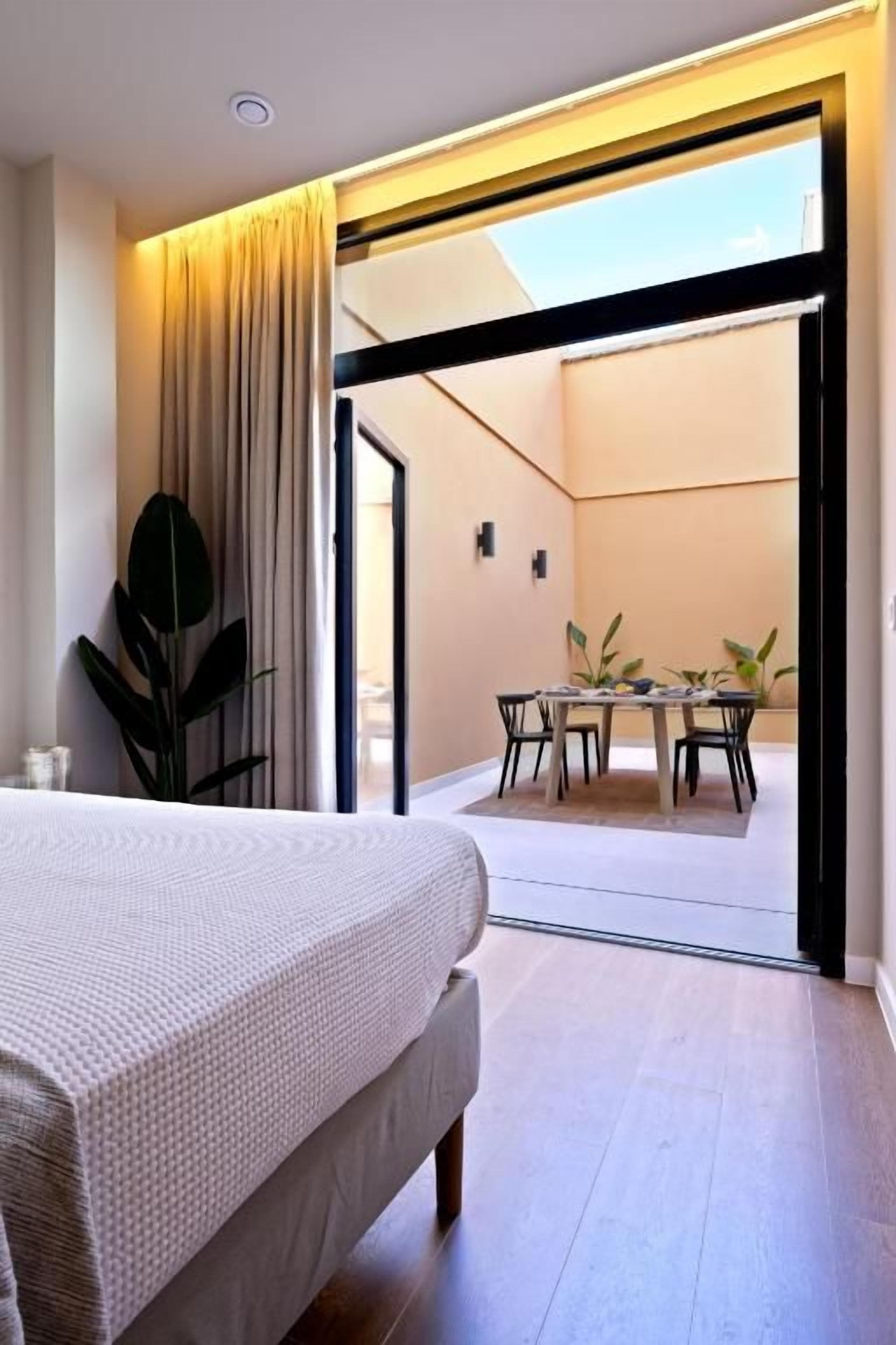 Un dormitorio con cama, un comedor con mesa y sillas, y vistas a un balcón por una puerta abierta.