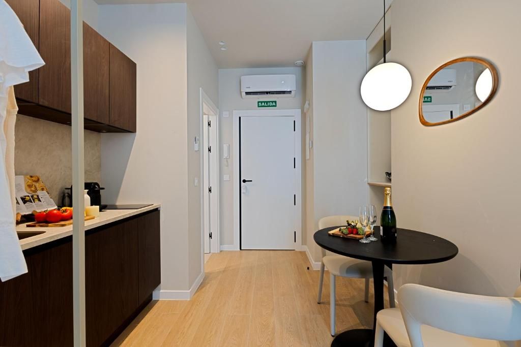 Cocina compacta con comedor, una puerta blanca con el rótulo 'SALIDA' y una mesa con una botella y vasos.