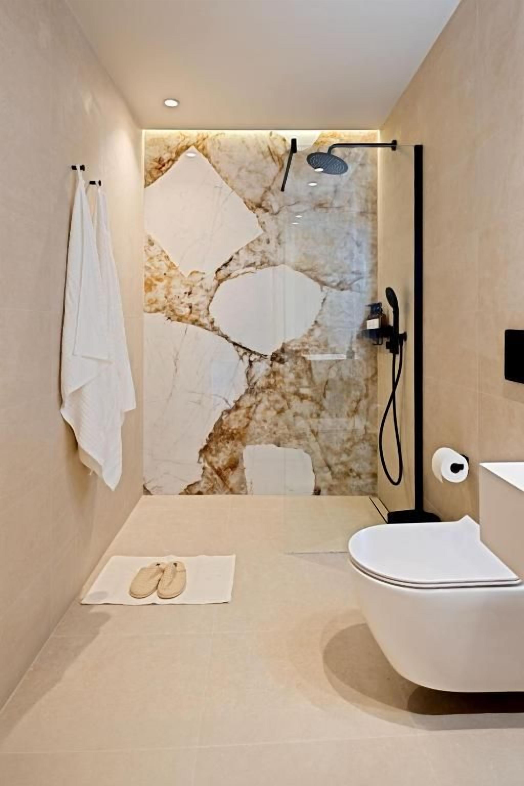 Ein modernes Badezimmer mit Marmorwand, einer Badewanne, einer Toilette und einer Duschkabine.