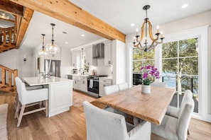 A modern kitchen with white cabinetry, a wooden dining table, and a large window with a view of the outdoors. - Coastal Vista (Santa Rosa Beach)