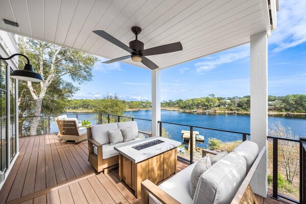 A covered outdoor deck with wooden flooring, a ceiling fan, and a view of a lake. - Coastal Vista (Santa Rosa Beach)