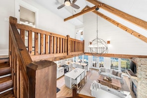 A spacious loft-style interior with a wooden staircase, a dining area, and a stone fireplace. - Coastal Vista (Santa Rosa Beach)